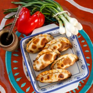 Plate of Argentine empanadas with traditional mate, red pepper, and green onions.